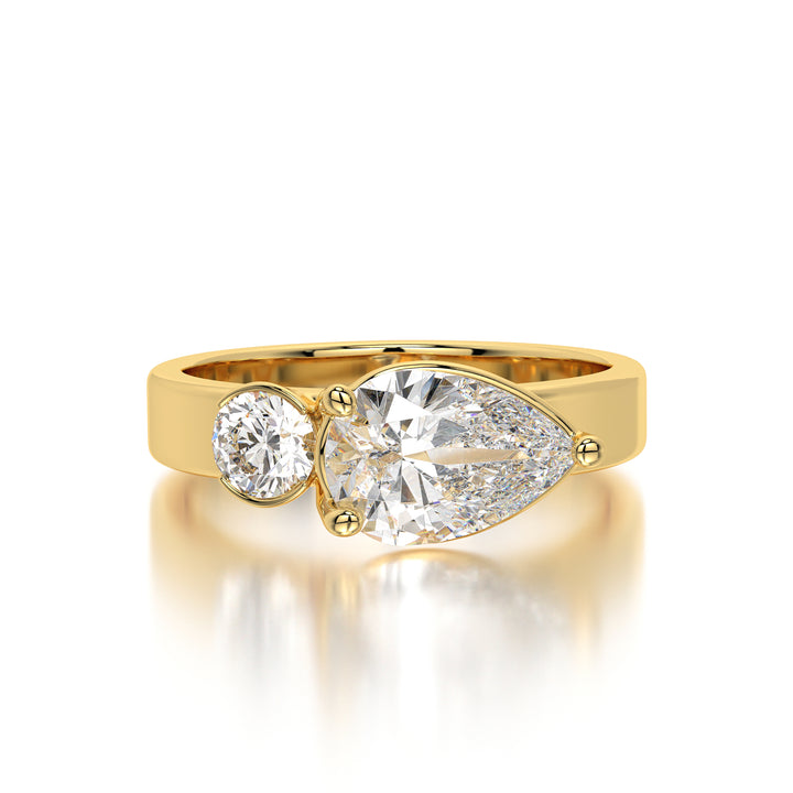 Front-facing image of a two-stone lab-grown diamond ring in 18K yellow gold, featuring a 1.35 carat pear-shaped solitaire with VS1 clarity and F color. Close-up shot showing the contrasting 0.55 carat round diamond in E color, reflecting brilliance and balance